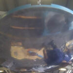 A factory worker inside the massive, concave stainless steel component of a spherical bearing, polishing its surface to demonstrate the scale of the manufacturing process.