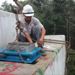 A worker secures a large Hercules POT Bearing on a bridge pier with assistance from a crane, showing a real-world application.