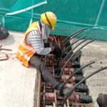 A construction worker in safety gear installing the tendons of a Hercules LMK post-tensioning system on a concrete bridge deck.