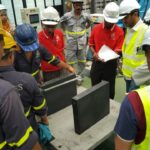 Engineers in safety gear conducting a quality control inspection on a finished elastomeric bearing pad.