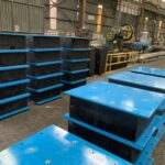 Blue manufacturing molds and equipment for producing elastomeric bearings in a workshop.