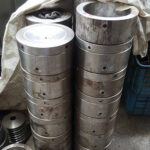 Stacks of heavy, machined steel cylinders ready for assembly into various types of bridge construction equipment.