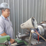 A skilled technician machining a precision steel component for a piece of custom bridge construction equipment.
